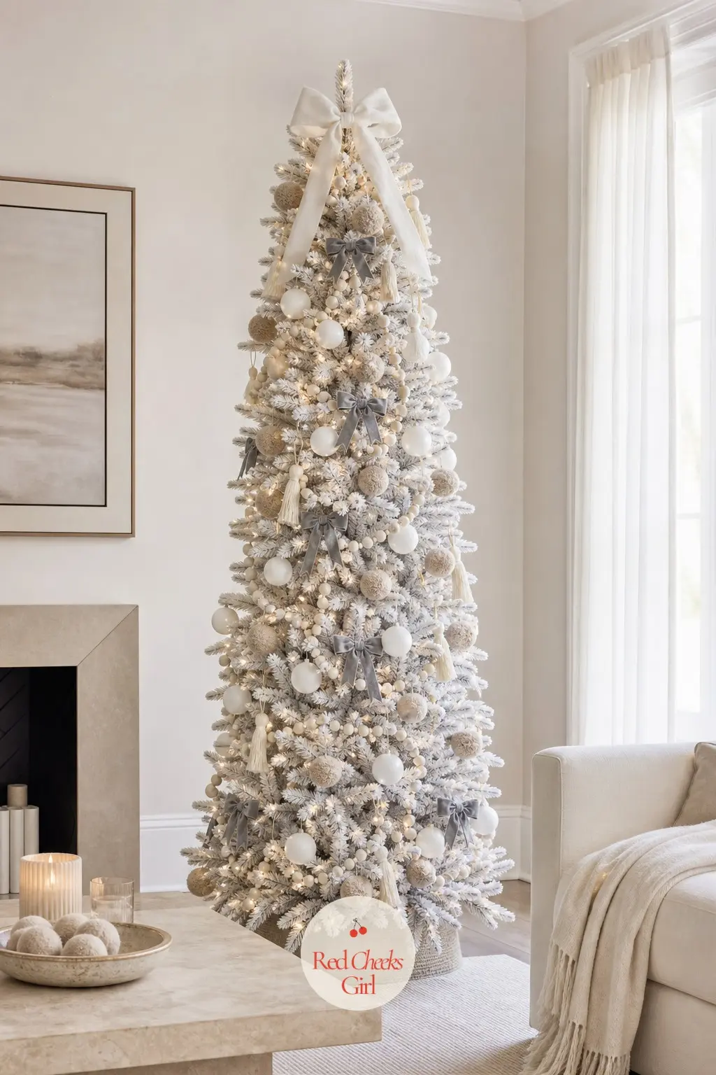 A Cashmere-Soft Pencil Tree in Oatmeal and Dove Grey — A slim artificial tree beside a low travertine table, felt pompoms standing in for the cashmere throw