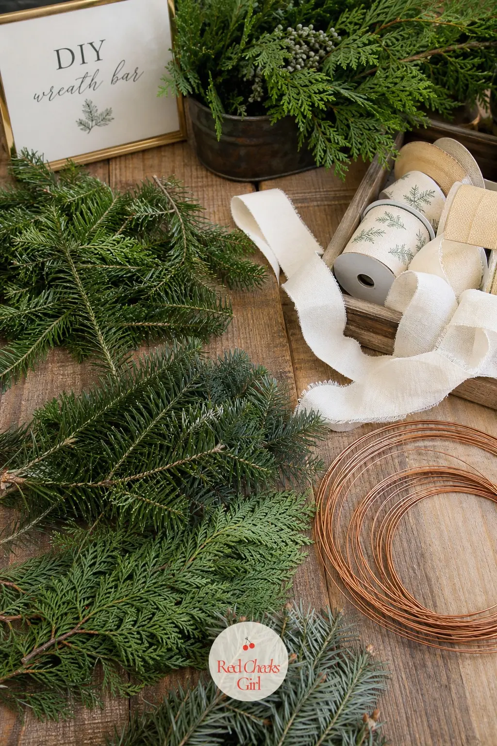 A DIY Wreath Bar with Pine Sprigs, Ribbon Spools and Wire Rings — A side table laid with loose pine sprigs, a few spools of cream ribbon and a stack of bare