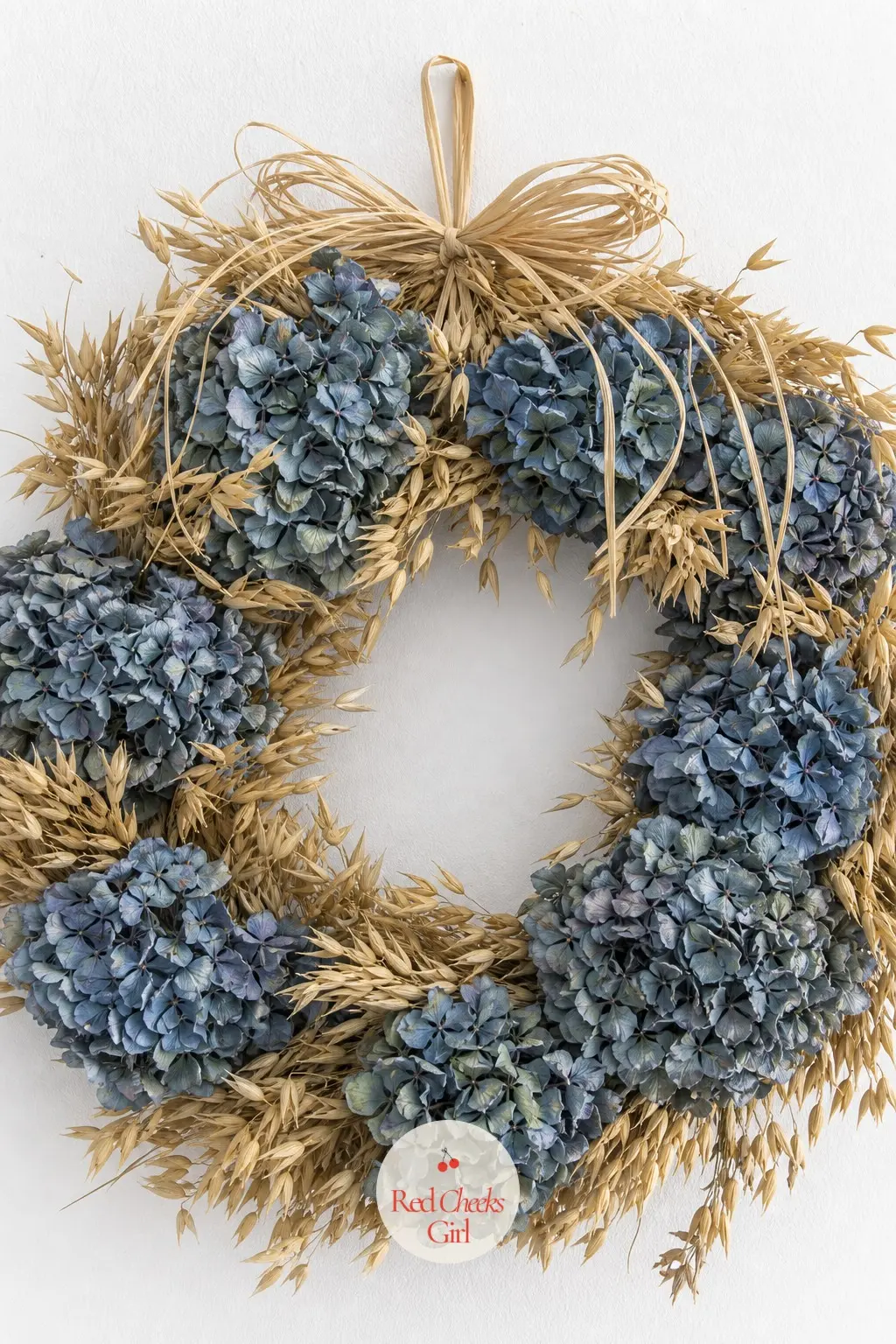 Slate Blue Hydrangea and Dried Oat Wall Wreath — Faded slate blue hydrangea heads, the kind that look almost grey at the edges, sit against golden dried oat